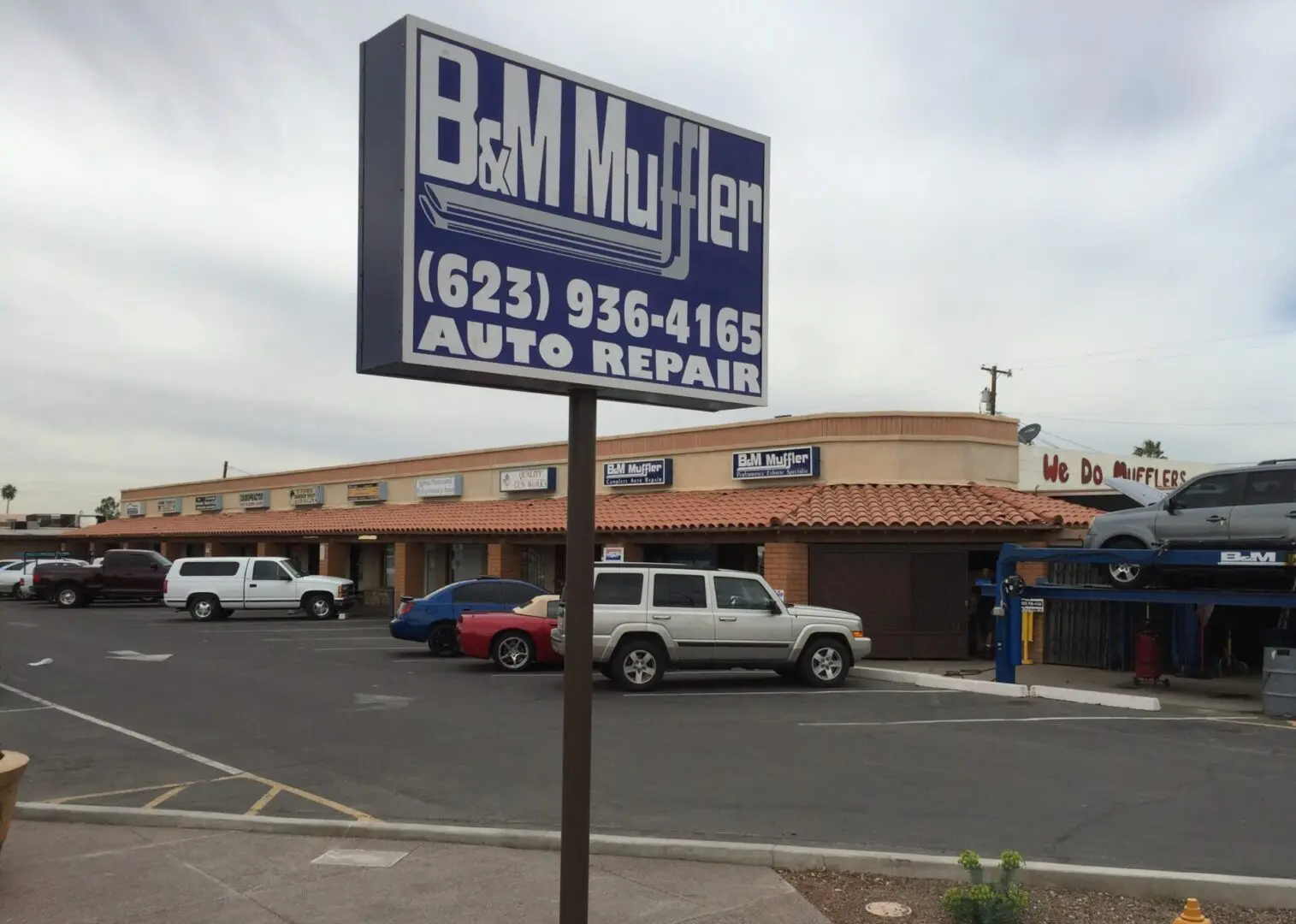 A sign for b & m muffler in front of an auto repair shop.